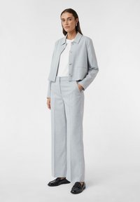 Lichtgrijze cropped jas met een kraag en knoopsluiting, gecombineerd met bijpassende hoge broek met brede pijpen en zwarte instappers.