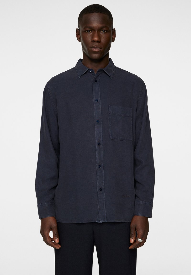 Navy blue long-sleeve shirt in a soft fabric with a chest pocket and button-up design. Features a collar and subtle stitching details.