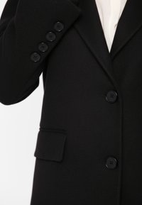 Zwarte blazer met een gestructureerde afwerking, voorzien van een borstzak, vijf zwarte knopen aan de mouw en een revers met inkeping.