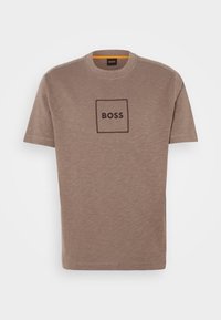 Brun bomulls t-skjorte med rund hals. Har en firkantet logo med "BOSS" i midten. Korte ermer og en jevn tekstur.
