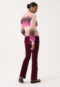 Gestrickter Pullover in einem Farbverlauf von Pinktönen, kombiniert mit bordeauxfarbenen Cordhosen im Schlag. Sanfte Texturen mit gerippten Bündchen und lockerer Passform.