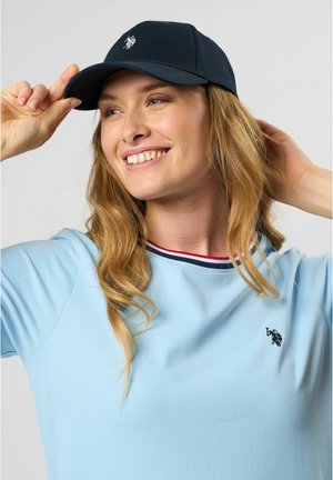 Baumwollmütze in Marineblau mit einem gebogenen Schirm, versehen mit einem gestickten Logo. Das Modell trägt ein hellblaues Hemd mit einem rot und marineblauen gestreiften Kragen.