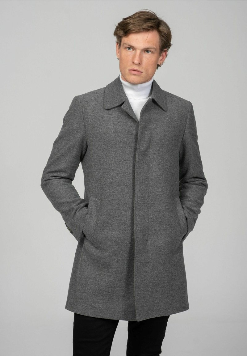 Grijze wollen blend jas met een rechte snit, opstaande kraag en zijzakken. Draag deze over een witte coltrui en in combinatie met zwarte broek.