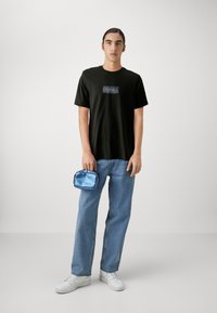 Camiseta negra de manga corta con un gráfico rectangular colorido, bolso de satén azul claro, jeans azul claro y zapatillas blancas.