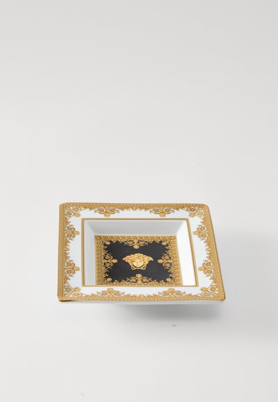 Štvorcový porcelánový tanier so čiernym stredom a zlatým emblémom Medusy, ozdobné zlaté a biele kvetinové okraje. Hladký, lesklý povrch.