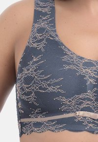 Niebieski biustonosz ozdobiony koronką z teksturowanym wzorem, półprzezroczystą tkaniną i miękkim różowym paskiem. Posiada falowane krawędzie i ramiączka na ramiona.