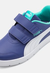 Chaussures synthétiques violettes avec des accents blancs, des sangles Velcro, un col rembourré et une doublure turquoise. Présentent une surface texturée et un design sportif.