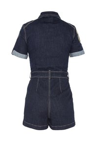 Tuta in denim blu scuro con maniche corte, polsini arrotolati, vita con cintura e cuciture a contrasto. Presenta una toppa sulla spalla sinistra.