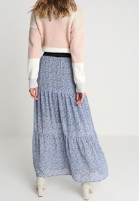 Jupe maxi bleu clair avec un imprimé floral, volants en couches et une taille élastique noire, associée à un pull court tricoté rose et blanc.