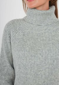 Pull à col roulé gris clair côtelé en matériau doux, avec un design ajusté et un col haut. Surface texturée avec un motif subtil.