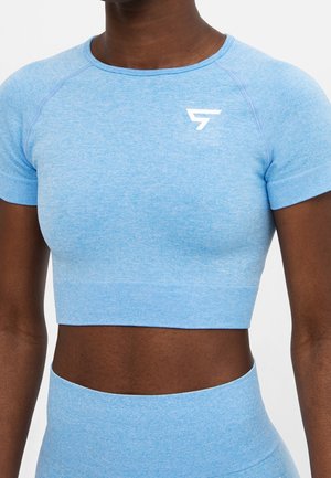 Close-up van een persoon die een aangesloten lichtblauwe crop top met korte mouwen draagt en bijpassende hooggetailleerde legging met wit logo op de borst.