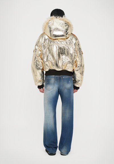 Gouden metallic pufferjack met een met bont gevoerde capuchon, geribbelde manchetten, gecombineerd met lichtblauwe denim jeans met een vervaagde wassingen.