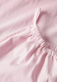 Tissu rose clair avec une texture douce, présentant un élastique froncé au niveau du cou et des bretelles fines. Détail en gros plan du matériau.