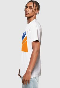 Hvid bomulds T-shirt med et stort orange og blåt Fanta-logo på fronten. Korte ærmer og en afslappet pasform.