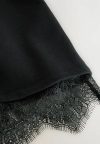 Ourlet en tissu noir avec un délicat galon en dentelle florale, présentant un fin maillage et des bords pointus sur un fond clair.