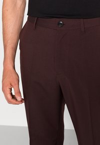 Bordeauxkleurige broek met een gladde textuur, voorzien van een knoopsluiting, riemlussen en zijzakken, taps toelopende vorm met minimaal stiksel.
