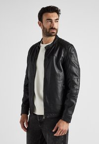 Schwarze Lederjacke mit Reißverschluss vorne, gerippten Schultern und Seitentaschen. Weiche Textur mit Nahtdetails und minimalistischem Design.