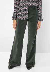 Pantalons en velours côtelé verts à jambes larges avec une texture lisse, dotés d'une taille cintrée et de poches latérales, associés à un haut à manches longues à motif.