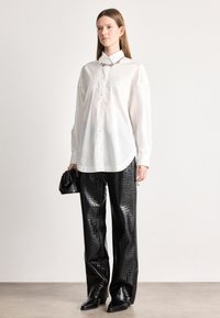 Λευκό πουκάμισο με κοφτό γιακά, συνδυασμένο με γυαλιστερό μαύρο παντελόνι με σχέδιο κροκοδείλου και μαύρες μπότες με τακούνι. Μικρή τσάντα στο χέρι.