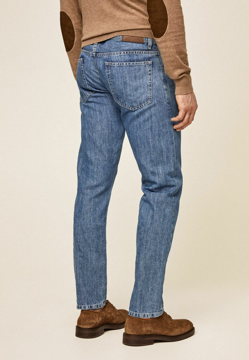 Jeans de mezclilla azul con corte recto, que cuentan con dos bolsillos traseros y un parche de cuero marrón en la cinturilla. Textura suave, diseño casual.