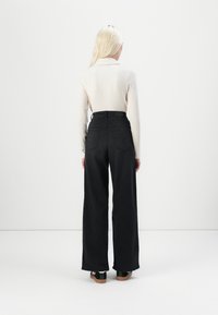 Black wide-leg jeans with back pockets, paired with a light ribbed long-sleeve top. Smooth, textured fabric, featuring a high waist design.