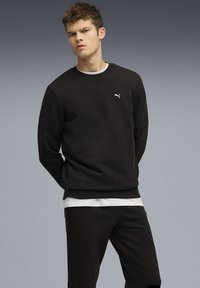 Sort sweatshirt med rund hals, hvid indvendig krave og lille logo patch på brystet. Glat stof og normal pasform.