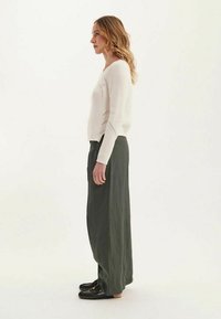 Jupe longue vert olive associée à un pull en tricot blanc, arborant un motif texturé et une coupe ample. Des chaussures noires complètent la tenue.