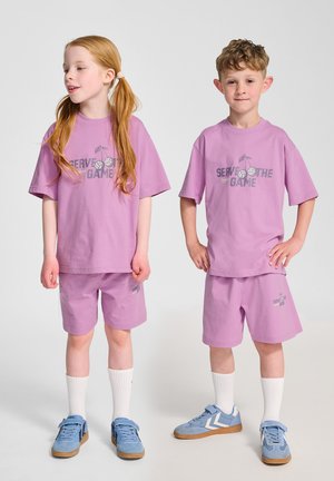 To børn har matchende løstsiddende lilla bomulds t-shirts og shorts med et "Serve the Game" grafik. Sneakers og hvide sokker fuldender looket.