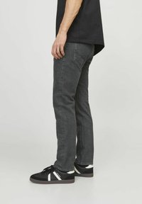 Grå denim jeans med en lige pasform, der har en falmet tekstur og to baglommer. Sat sammen med sorte sneakers med hvide detaljer.