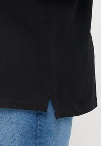 Sort bomulds T-shirt med lige kant og sideslids, parret med lyseblå denim jeans. Fremtrædende tekstur synlig på stofoverfladen.