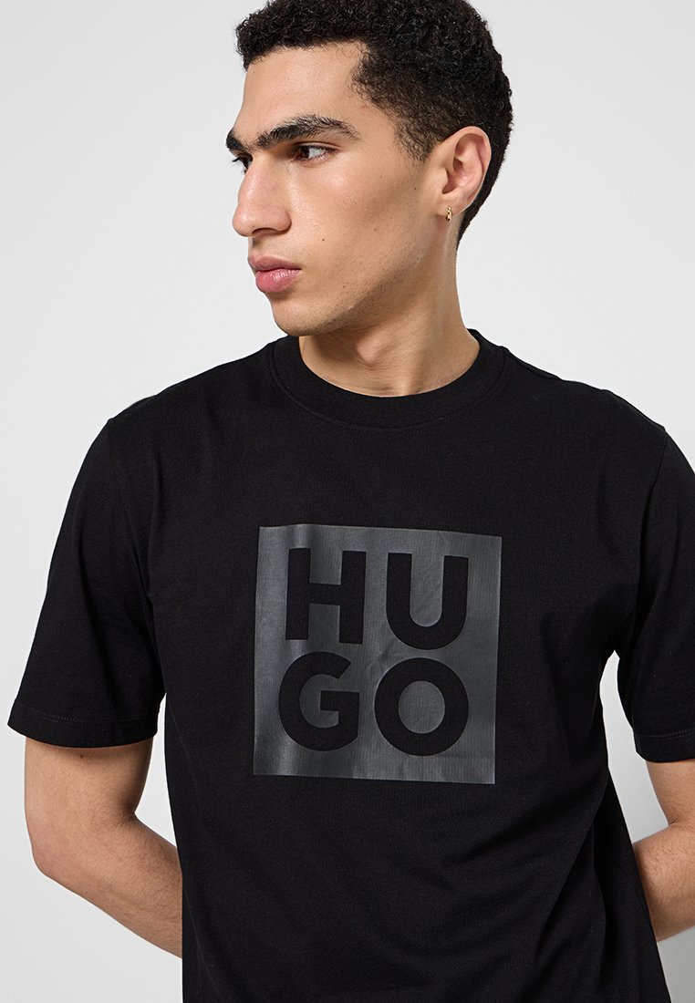 T-shirt en coton noir avec un grand logo "HUGO" noir mat imprimé sur le devant. Design à col rond avec des manches courtes.