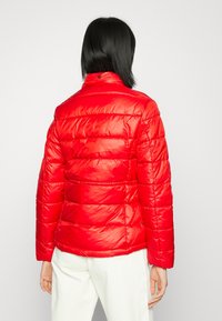 Röd vadderad pufferjacka med hög krage, med en glänsande, slät textur och horisontell söm. Enkel design, inga synliga logotyper.