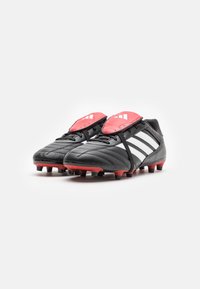 Chaussures de football noires avec accents rouges et rayures blanches. Dotées d'une tige en cuir texturé, d'une languette rembourrée et de crampons moulés sur la semelle extérieure.