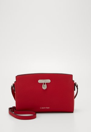 Sac bandoulière en cuir rouge texturé avec détail de serrure argentée à l'avant et bandoulière réglable, logo Calvin Klein au centre en bas.