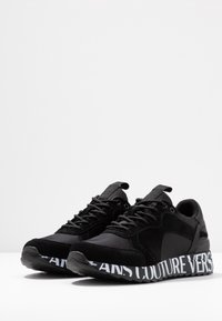 Svarta sneakers med en blandning av mocka och syntetiskt material. Texturerad sula med framträdande vit branding längs mellansulan. Rund tådesign.