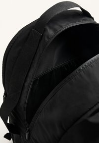 Fekete hátizsák, puha szövetborítással, cipzáras tetejével és hálós zsebbel. Állítható pántokkal és minimalista dizájnnal, látható fémhardver nélkül.