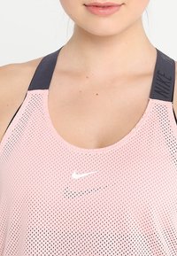 Canotta in mesh traspirante di colore rosa chiaro, con scollatura a giro e spalline nere. Presenta un logo Nike bianco e un motivo testurizzato.