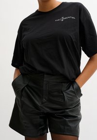 Svart bomullströja med vit text, kombinerad med högmidjade svarta lädershorts med sidofickor och en slät, glänsande yta.