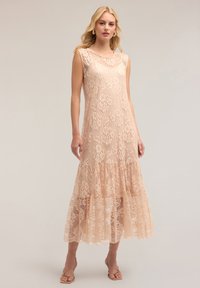 Lange kanten jurk in zachte blush, met ingewikkelde bloemenpatronen, korte mouwen en een gelaagde rand. Zachte textuur met een vloeiende silhoutte.
