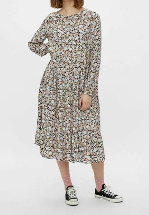 Robe florale à manches longues avec une base noire, des fleurs multicolores, une jupe plissée et un col rond, associée à des baskets noires et des chaussettes roses.