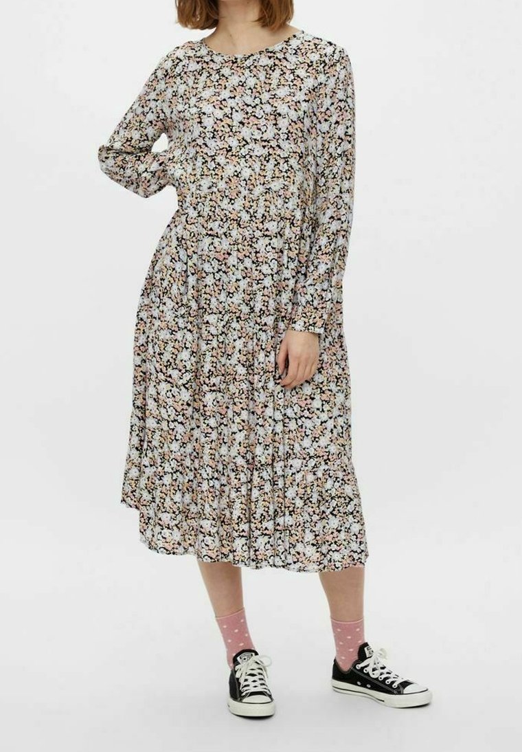 Långärmad blommig klänning med svart bas, flerfärgade blommor, plisserad kjol och rund halsringning, i kombination med svarta sneakers och rosa strumpor.