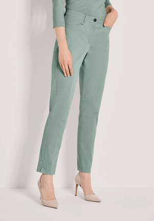 Mintgroene op maat gemaakte broek van zachte stof, met een aansluitend ontwerp, steekzakken aan de voorkant en een enkele knoopsluiting, gecombineerd met beige hakken.