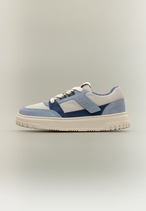 Zapatilla baja en ante crema, azul claro y azul marino con cordones blancos y una suela gruesa de caucho color blanco roto.