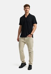 Black short-sleeve shirt with a textured pattern, paired with light beige pants and black sneakers. The shirt has a relaxed fit and buttons.