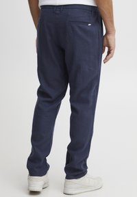 Pantalonii din bumbac navy cu amestec au un croi drept, buzunare la spate cu detalii din clapeta și sunt asortați cu adidași albi.