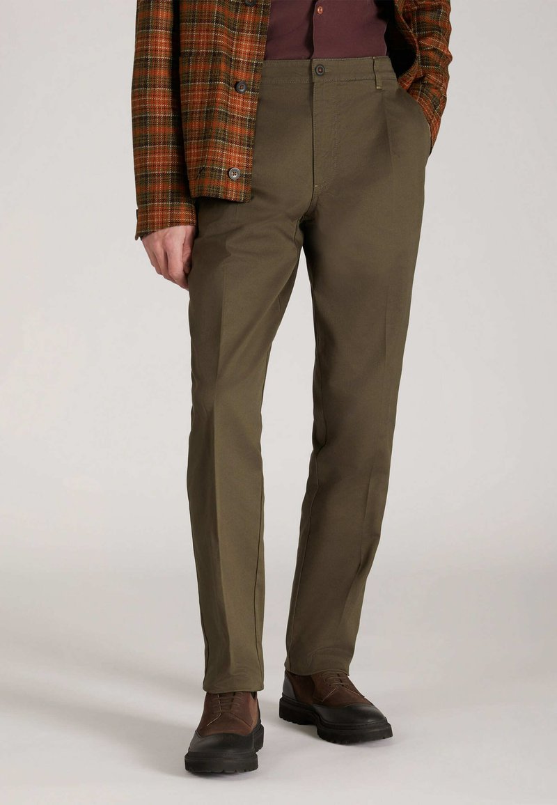 Olijfgroene broek met een gladde textuur en rechte pijpen, voorzien van voorzakken en een knoopsluiting, gedragen met bruine schoenen.