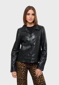 Černá kožená bunda s límcem, čtyřmi knoflíky a dlouhými rukávy. Nosená s kalhotami z leopardího vzoru, které mají hladkou, lesklou texturu.