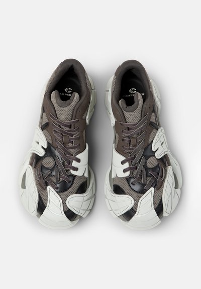 Baskets épaisses en maille grise avec des accents brun foncé et des semelles blanches épaisses segmentées, vues de dessus sur un fond blanc.