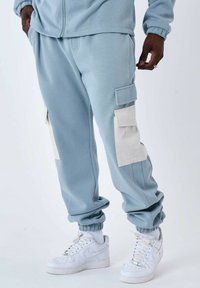Pantaloni jogger azzurri chiari in cotone, con tasche cargo laterali con accenti crema. Polsini elasticizzati e vestibilità comoda. Abbinati a sneakers bianche.