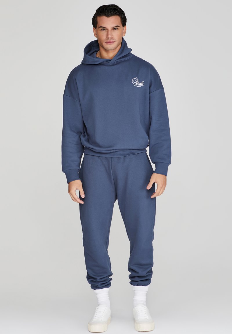 Conjunto de sudadera con capucha y joggers en azul marino, hecho de una tela suave, presenta un ajuste relajado, puños acanalados y un pequeño logotipo en el pecho.